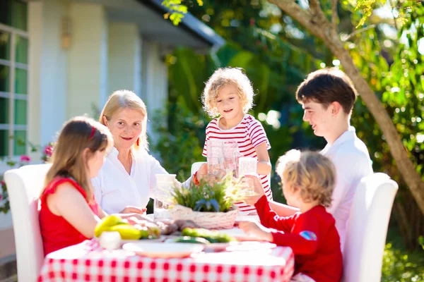 屋外で食べる家族 庭の夏の楽しみ 日当たりの良い裏庭でバーベキュー おばあちゃんと子供たちは屋外デッキで昼食を食べます 両親や子供たちはBbqをお楽しみください 男の子と女の子とともにお母さん — ストック写真