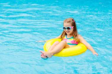 Yüzme havuzunda yüzen bir çocuk. Çocuklar yüzer. Küçük çocuklar için renkli sarı yüzer. Küçük kız yaz tatilinde tropikal tatil köyünde eğleniyor. Plaj ve su oyuncakları. Güneş koruması.