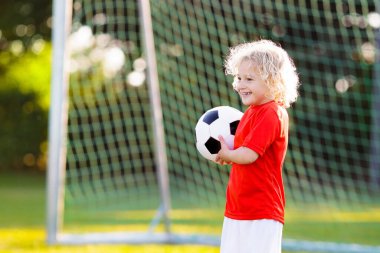 Çocuklar dışarıda futbol oynarlar. Çocuklar futbol maçında gol attılar. Küçük çocuk topa vuruyor. Formalı ve kramponlu koşan çocuk. Okul futbol kulübü. Genç oyuncu için spor eğitimi.