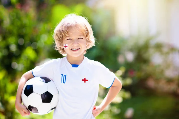 England football fan cheering. Kids play soccer and celebrate victory on outdoor field. England team supporter. Little boy in English jersey and cleats kicking ball. Sports training for children.