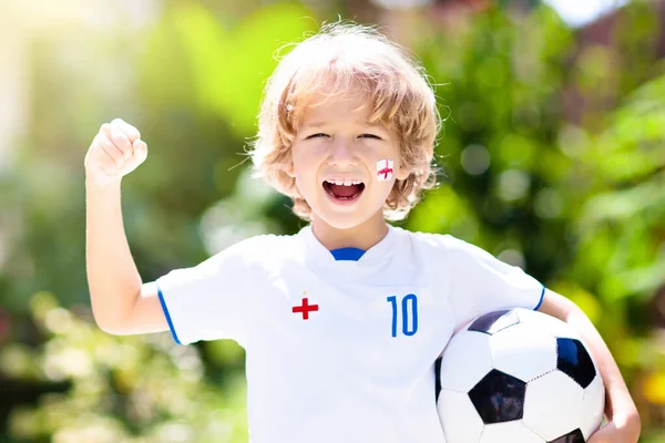 England football fan cheering. Kids play soccer and celebrate victory on outdoor field. England team supporter. Little boy in English jersey and cleats kicking ball. Sports training for children.