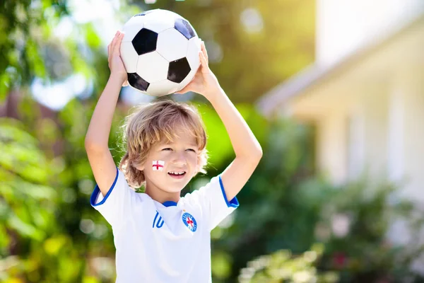 England football fan cheering. Kids play soccer and celebrate victory on outdoor field. England team supporter. Little boy in English jersey and cleats kicking ball. Sports training for children.