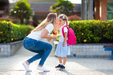 Anne ve çocuklar okuldan sonra. Anaokulundan ya da anaokulundan sonra çocukları alan genç bir anne. Öğrencileri toplayın. Oğlan ve kız okul bahçesinde ailelerine koşuyorlar..