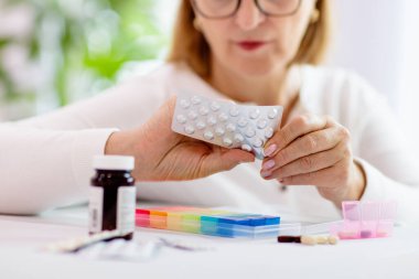 Kıdemli hasta için ilaç kutusu. İlaç konteynırı. Ağrı kesici ve hastalık tedavisi için ilaç kullanan yaşlı bir kadın. Hasta, emekli, uyuşturucu bağımlısı kadın. Sağlıklı emeklilik için günlük vitaminler.