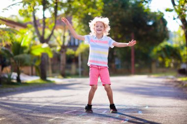 Çocuklar yaz parkında seksek oynuyor. Sağlıklı aktif açık hava oyunu. Banliyö caddesinde tebeşirle oynayan ve çizen çocuklar. Erkek ve kız zıplıyor. Küçük çocuk için viski eğlencesi. Çocuk atlaması.