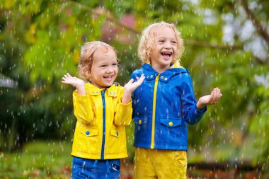 Çocuklar Sonbahar yağmur altında oynar. Yağmurlu günde açık oynayan çocuk. Yağmur alıcı küçük çocuk ağır duş altında bırakır. Güz fırtınası'nda bir park. Su geçirmez giymek için çocuk. Çocuklar açık havada tarafından herhangi bir hava.