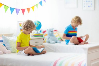 Çocuk yatakta kitap okuyor. İki çocuk için yatak odası. Küçük çocuklar beyaz yatakta renkli yataklı kitaplar okurlar. Çocuk yuvası. Küçük kardeşler içeride oynarlar. Şekerleme ve uyku zamanı. Ödev yapan öğrenci.
