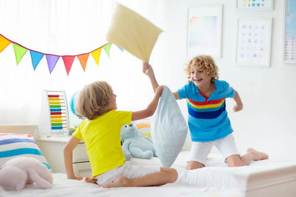 孩子们枕头大战家庭的乐趣 两个孩子的卧室 有五颜六色的床上用品和大窗户 小男孩在屋里嬉笑玩耍 兄弟们一起玩带双人床的客房 — 图库照片