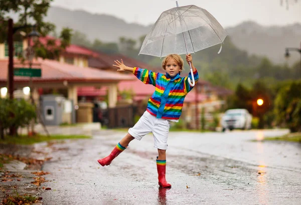 秋の雨の中で遊ぶ子供 傘を持ってる子供 秋に街を走る少年 どんな天気でも子供のための屋外の楽しみ 子供のための雨防水摩耗 ブーツやジャケット — ストック写真