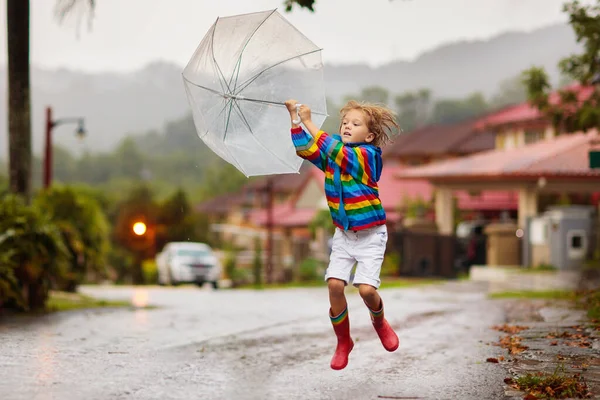 秋の雨の中で遊ぶ子供 傘を持ってる子供 秋に街を走る少年 どんな天気でも子供のための屋外の楽しみ 子供のための雨防水摩耗 ブーツやジャケット — ストック写真