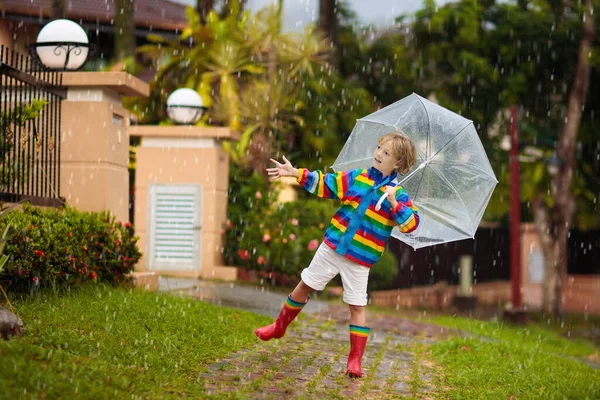秋の雨の中で遊ぶ子供 傘を持ってる子供 秋に街を走る少年 どんな天気でも子供のための屋外の楽しみ 子供のための雨防水摩耗 ブーツやジャケット — ストック写真