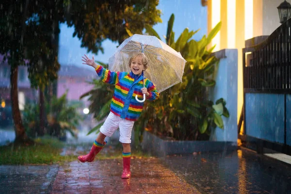 秋の雨の中で遊ぶ子供 傘を持ってる子供 秋に街を走る少年 どんな天気でも子供のための屋外の楽しみ 子供のための雨防水摩耗 ブーツやジャケット — ストック写真