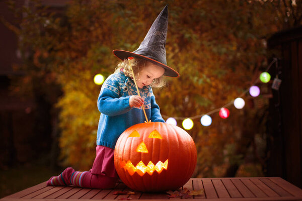 Kids trick or treat in Halloween costume. Children in colorful dress up with candy bucket on suburban street. Little girl trick or treating with pumpkin lantern. Autumn holiday fun.