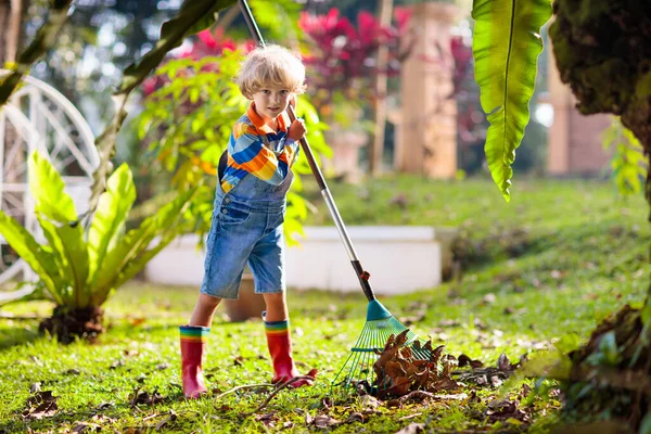 秋天花园的孩子和耙 秋天的时候 孩子们在挖树叶 在落叶季节播种 小男孩帮我打扫后院 草坪上的叶子堆 孩子们帮助做家务活 孩子们在户外玩耍 — 图库照片