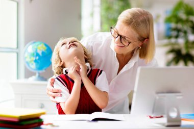 Çevrimiçi uzaktan öğrenme. Bilgisayarlı okul çocukları öğretmen ve sınıf grubuyla görüntülü konuşma yapıyorlar. Anne oğluna yardım ediyor. Çocuk evden ders çalışıyor. Koronavirüs salgınında evde eğitim.