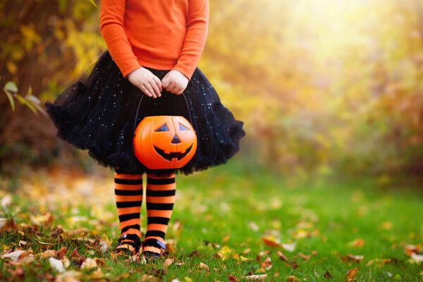 Little girl in witch costume playing in autumn park. Child having fun at Halloween trick or treat. Kids trick or treating. Toddler kid with jack-o-lantern. Children with candy bucket in fall forest.