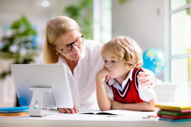 Çevrimiçi uzaktan öğrenme. Bilgisayarlı okul çocukları öğretmen ve sınıf grubuyla görüntülü konuşma yapıyorlar. Anne oğluna yardım ediyor. Çocuk evden ders çalışıyor. Koronavirüs salgınında evde eğitim.