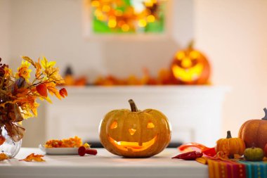 Cadılar Bayramı için balkabağı oyan bir kadın. Geleneksel şaka mı şeker mi dekorasyonu için önlüklü bir kadın Jack O feneri kesiyor. Altın sonbahar yapraklı şöminenin üzerinde çelenk olan dekore edilmiş oturma odası.