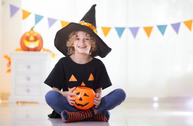 Cadılar Bayramı 'nda cadı kostümü giymiş küçük bir kız ve oğlan. Çocuklar balkabağı kovasında şeker tutuyorlar. Çocuklar Cadılar Bayramı 'nı süslü şöminede kutluyor. Aile şakası mı şeker mi.