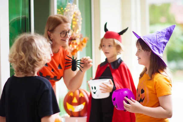 子供たちはハロウィーンの夜にトリックや治療します 装飾された家のドアの子供 魔女と吸血鬼の衣装とキャンディバケツとカボチャのランタンと帽子の男の子と女の子 お菓子のある女 — ストック写真