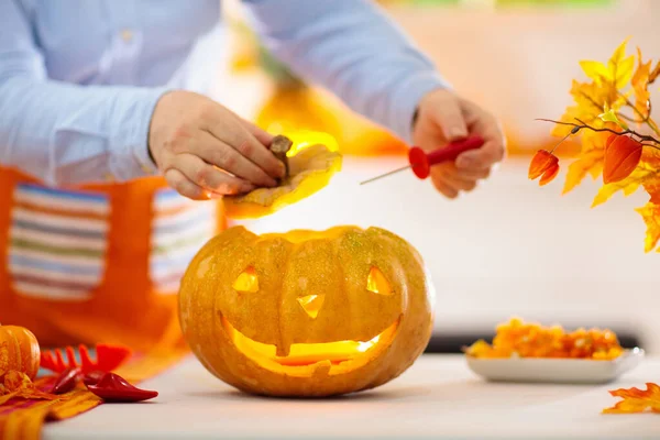 Cadılar Bayramı için balkabağı oyan bir kadın. Geleneksel şaka mı şeker mi dekorasyonu için önlüklü bir kadın Jack O feneri kesiyor. Altın sonbahar yapraklı şöminenin üzerinde çelenk olan dekore edilmiş oturma odası.