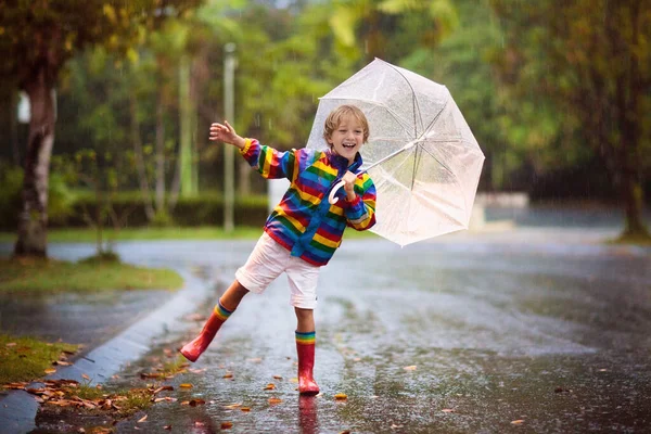 秋の雨の中で遊ぶ子供 傘を持ってる子供 秋に街を走る少年 どんな天気でも子供のための屋外の楽しみ 子供のための雨防水摩耗 ブーツやジャケット — ストック写真