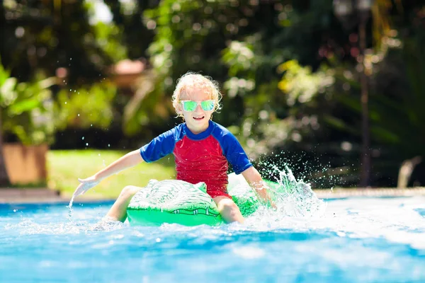 スイミングプールで遊ぶ子供 子供たちは泳ぐことを学ぶ 熱帯リゾートで夏休みに水遊びをする膨脹可能なおもちゃのフロートを持つ小さな男の子 ビーチの休日におもちゃのワニと子供 — ストック写真