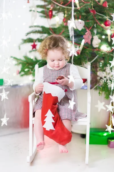 Linda niña sonriente revisando su media de Navidad bajo un árbol decorado —  Fotos de Stock