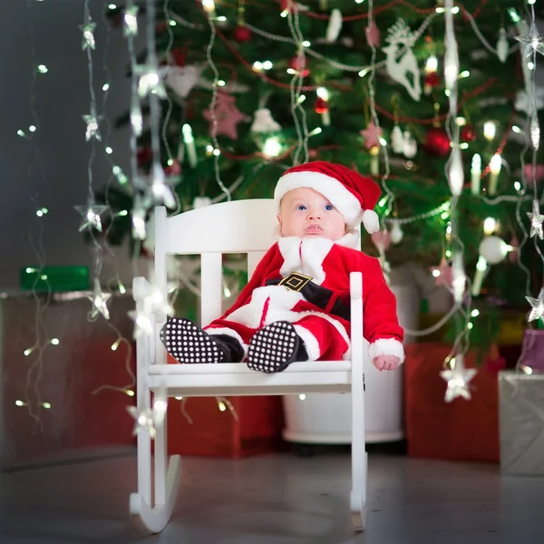 Söt newborn baby i santa dräkt i ett mörkt rum med vackra julgran — Stockfoto