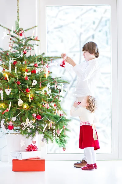 Bedårande barn girl att hjälpa sin bror att dekorera en julgran — Stockfoto