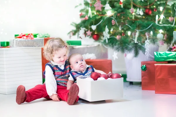 Little toddler girl and her newborn brother helping to decorate new year tree Royalty Free Stock Photos