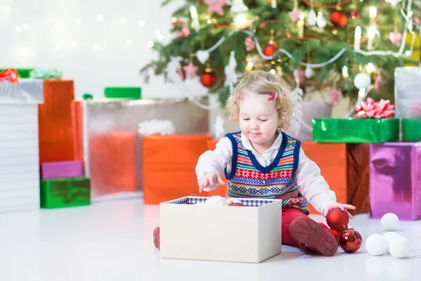 Portrait of a little toddler girl in a warm sweater under Christmas tree with present — Stock Photo, Image