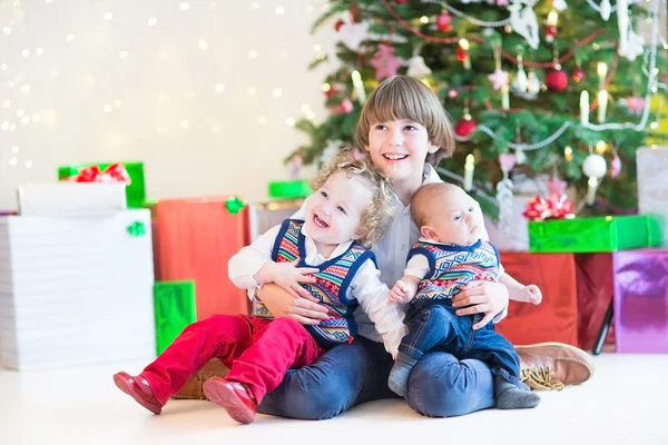 Tres niños felices sentados bajo un hermoso árbol de Navidad —  Fotos de Stock