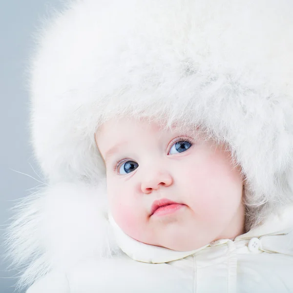 Bebê muito engraçado em um terno de neve branco e chapéu de pele grande — Fotografia de Stock