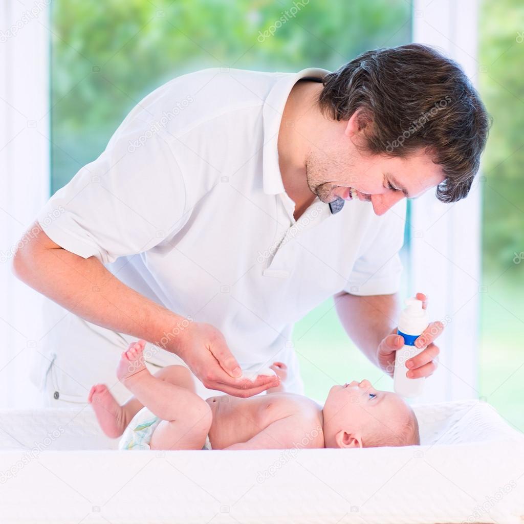 Young loving father changing diaper of his newborn baby son, hol