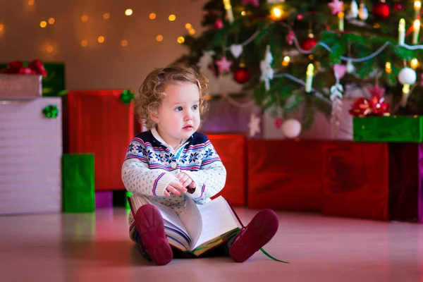 Klein meisje lezen op kerstboom — Stockfoto