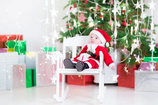 Cute newborn baby boy in Santa costume sitting under a Christmas tree — Stock Photo, Image