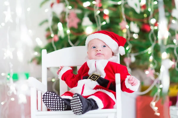 Menino recém-nascido em roupa de Papai Noel sentado sob uma árvore de Natal — Fotografia de Stock