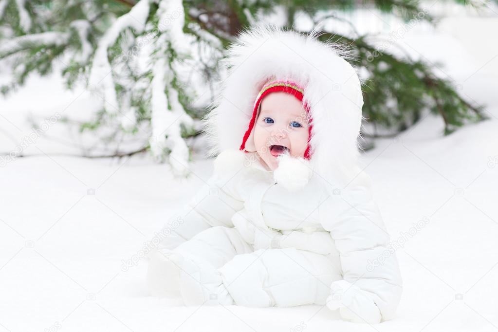 Adorable laughing baby sitting in snow under a Christmas tree