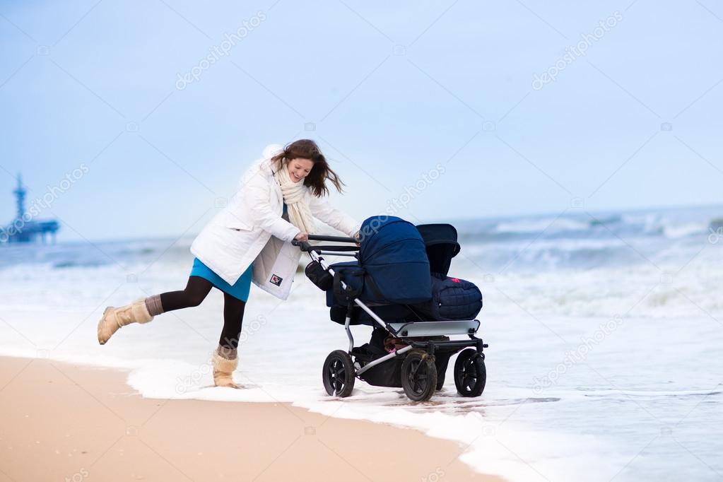 Happy active young mother walking on a beach pushing an all terrain double stroller