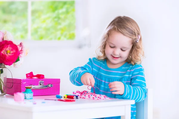 Kleines Mädchen näht ein Kleid für ihre Puppe — Stockfoto