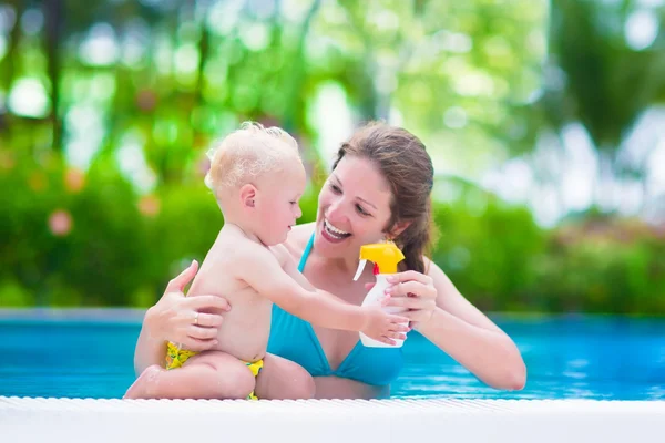 Mãe aplicando protetor solar no bebê na piscina — Fotografia de Stock