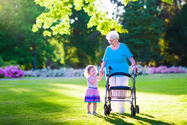 Senior lady with a walker and little girl in a park — Stock Photo, Image