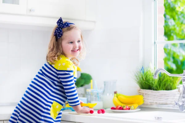 Lilla flickan förbereder frukost i ett vitt kök — Stockfoto