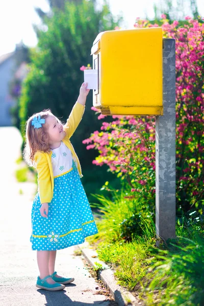 Kleines Mädchen mit einem Umschlag neben einem Briefkasten — Stockfoto