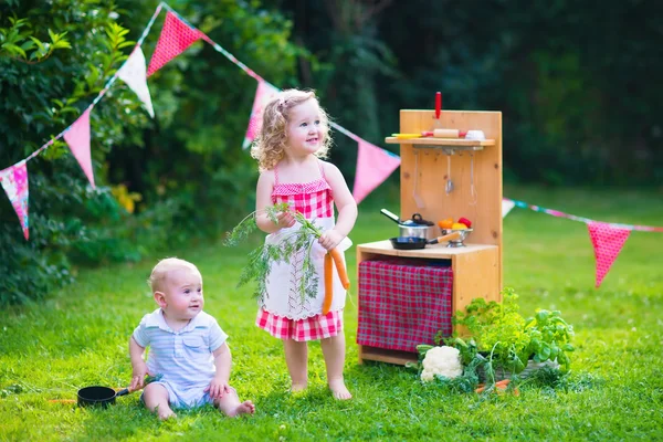 Niños jugando con una cocina de juguete en un jardín de verano — Foto de Stock