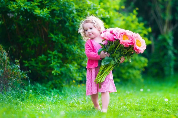 Kleines Mädchen mit Pfingstrosenblumen im Garten — Stockfoto