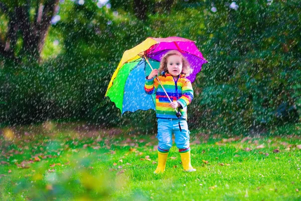 Mała dziewczynka gra w deszcz posiadający kolorowy parasol — Zdjęcie stockowe