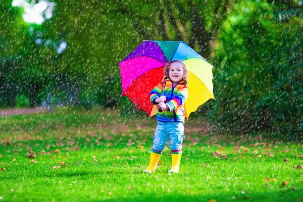 Mała dziewczynka gra w deszcz posiadający kolorowy parasol — Zdjęcie stockowe