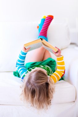 Küçük kız beyaz bir kanepede kitap okuma